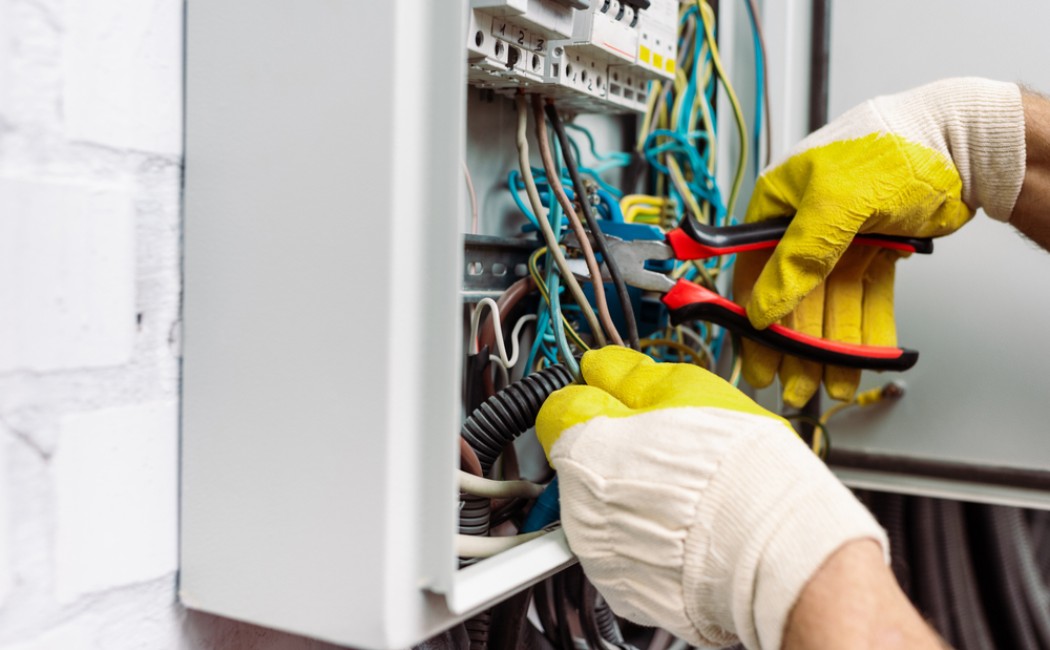 Electrical services specialist using insulated pliers to safely repair wiring inside an electrical breaker panel.