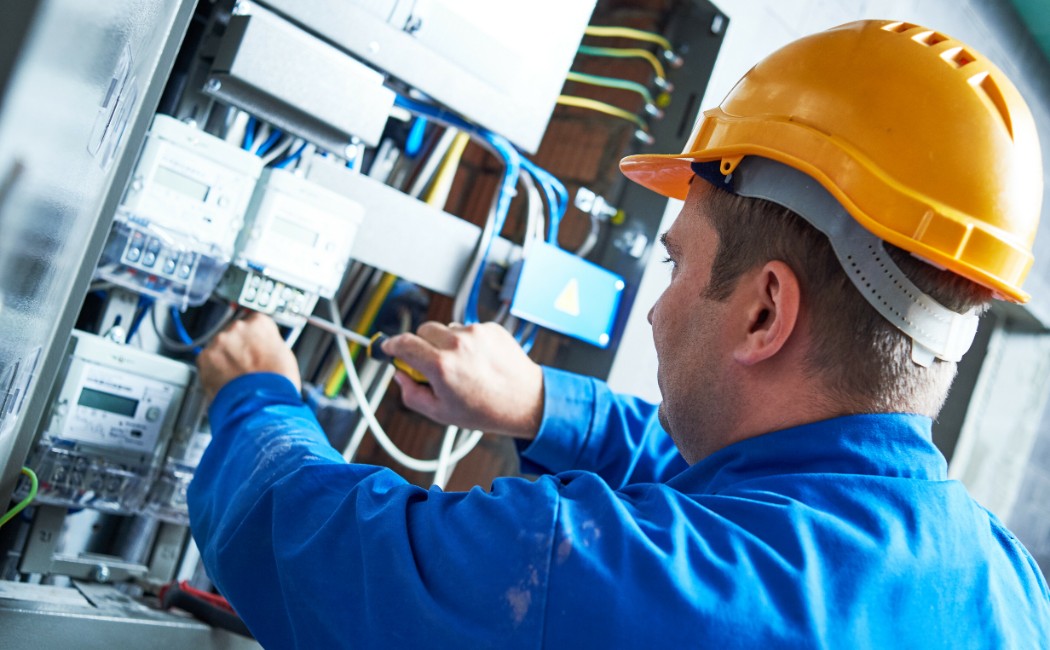 Electrical services expert repairing and wiring an electrical control panel while wearing protective safety gear.